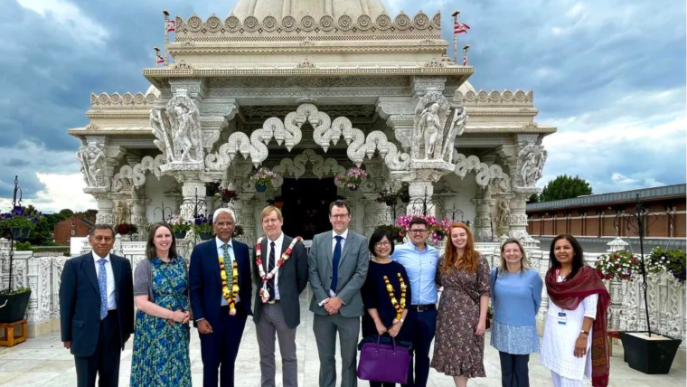 A group of people stand smiling in front of Neasden Temple