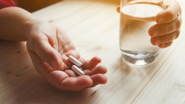 A senior woman's hand holding medication with a glass of water.